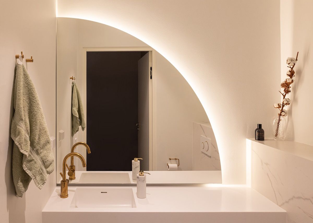 Lo sfondo dello specchio è illuminato da una striscia LED curva in un profilo di alluminio. La luce si apre all'intero spazio attraverso le pareti e il soffitto della stanza della luce.